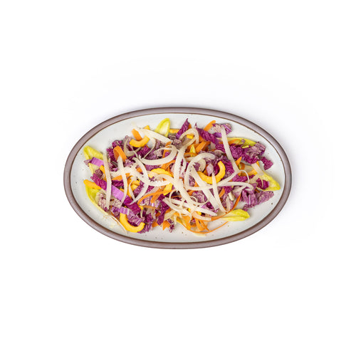 A medium oval ceramic platter in a cool white color featuring iron speckles and an unglazed rim, with cut onions and more