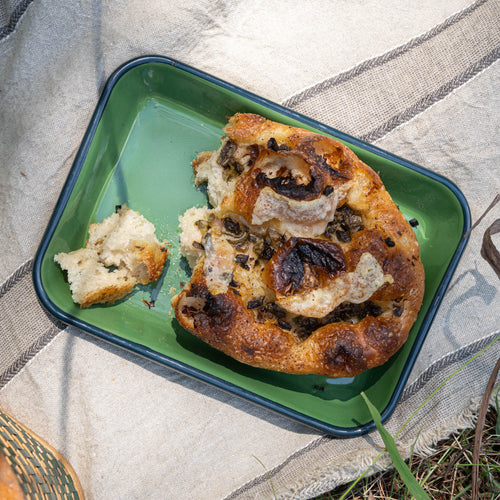 Large rectangular baking dish in a green color with a dark green rim, filled with an artful bread loaf on a tablecloth outside.