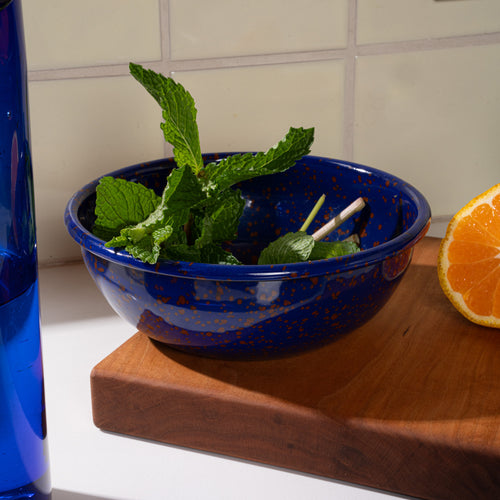 A medium enamel bowl in midnight blue color with red splatter pattern, filled with mint leaves.