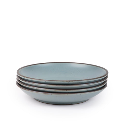 A stack of 4 large ceramic plates with a curved bowl edge in a blue-grey color featuring iron speckles and an unglazed rim.