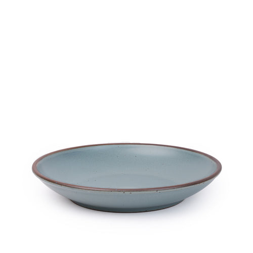 A large ceramic plate with a curved bowl edge in a blue-grey color featuring iron speckles and an unglazed rim.