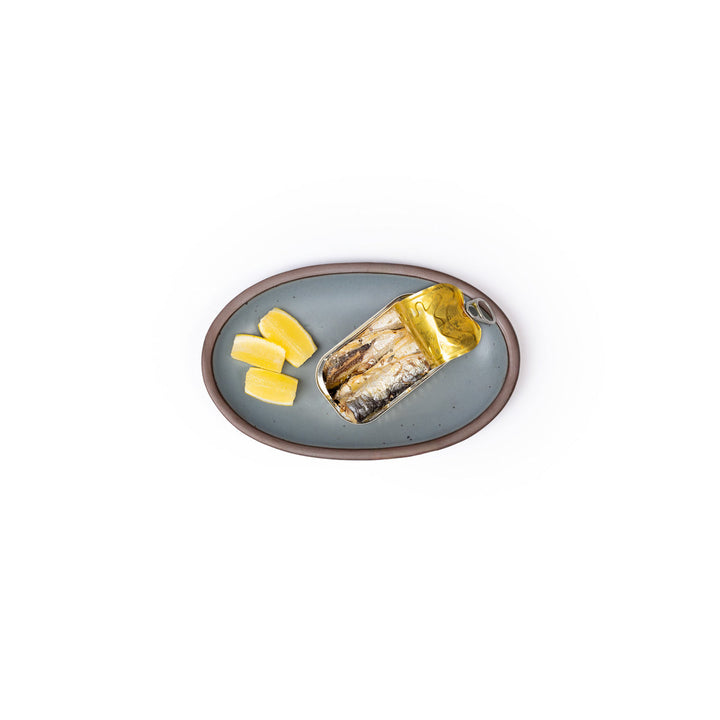 A small oval platter with three lemon wedges and a open can of sardines