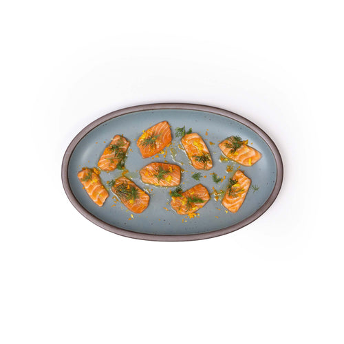 A medium oval ceramic platter in a blue-grey color featuring iron speckles and an unglazed rim, with salmon