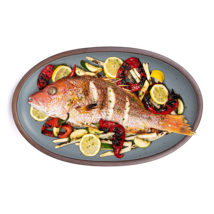 An oval platter with a red snapper surrounded by veggies