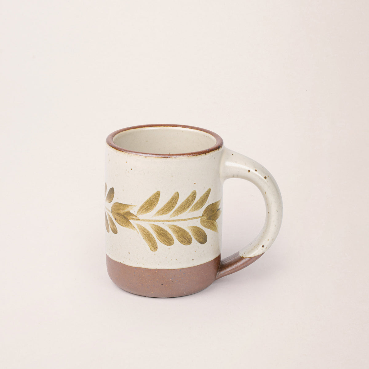 Warm off-white ceramic mug with a hand-painted olive green leaf motif and exposed clay base on a plain white background.