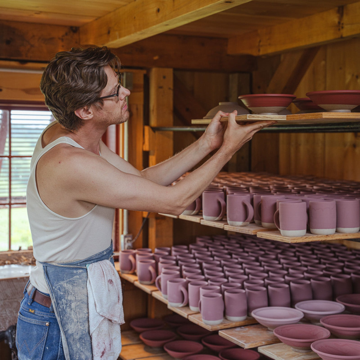 John holding up a tray of ceramic pots, glazed and ready to be fired, in his pottery studio.