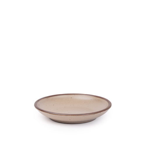 A small ceramic plate with a curved bowl edge in a warm pale brown color featuring iron speckles and an unglazed rim.