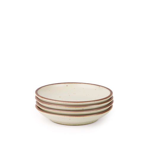 A stack of 4 small ceramic plates with a curved bowl edge in a warm off-white color featuring iron speckles and an unglazed rim.