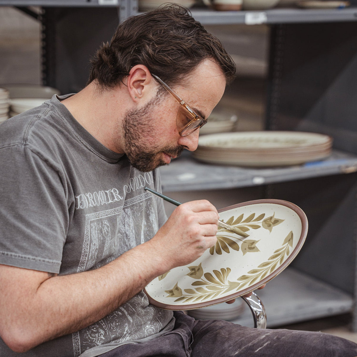 Alex handpainting a ceramic platter in a workshop studio setting