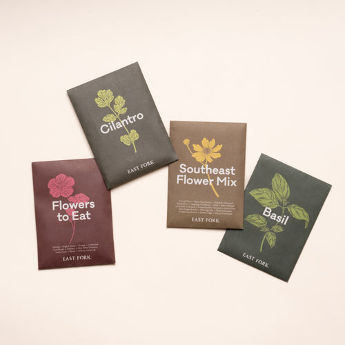 Collection of East Fork seed packets labeled Cilantro, Flowers to Eat, Southeast Flower Mix, and Basil arranged on a light background.