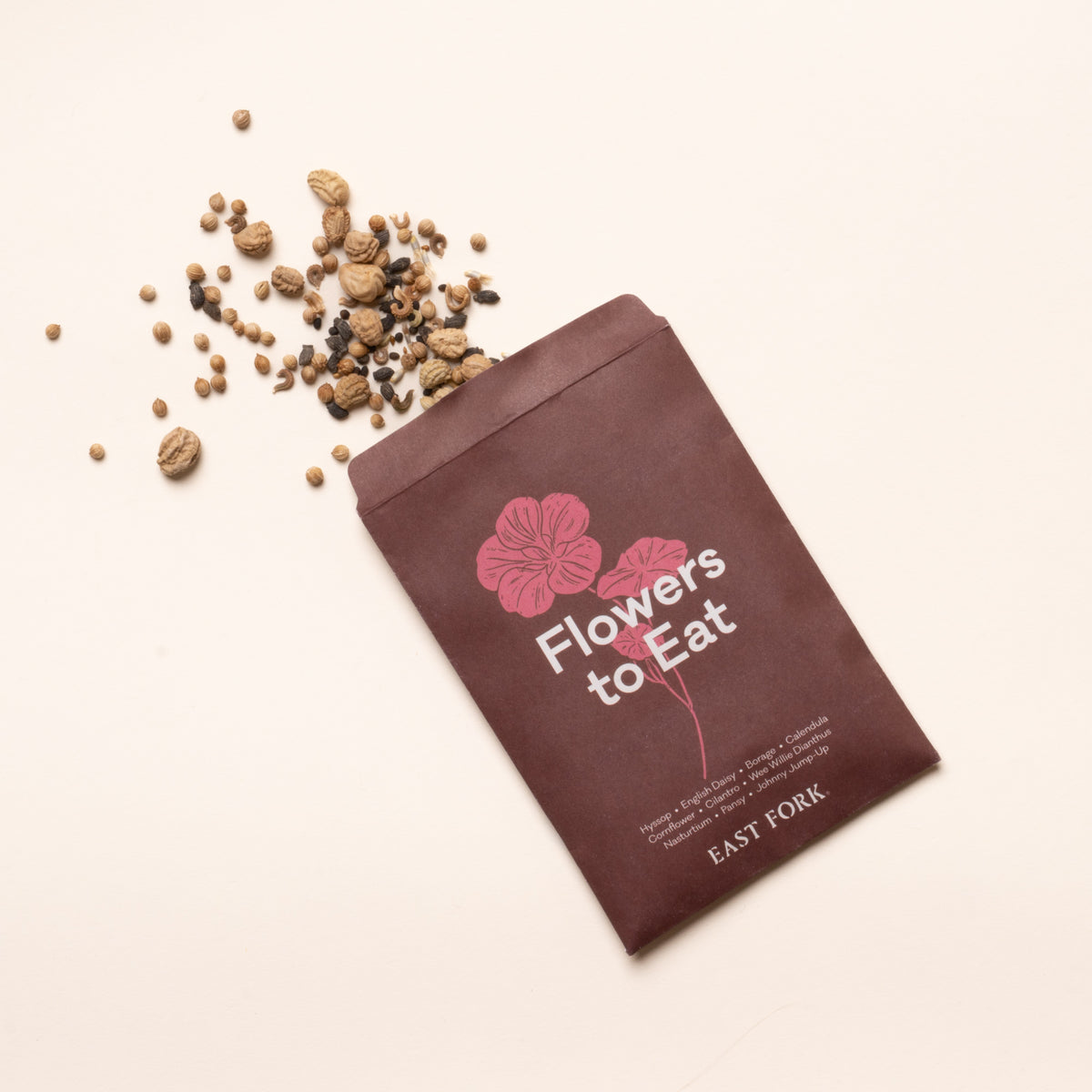 Flowers to Eat seed packet with pink floral illustration and mixed flower seeds scattered on a light background.