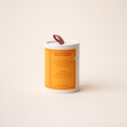 RAAZI Indian Breakfast tea tin with a bright orange label and red pull tab, photographed on a soft neutral backdrop.