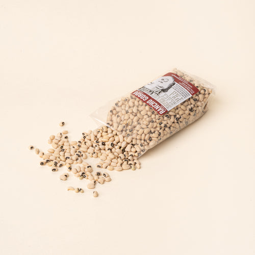 Bag of Rancho Gordo Super Lucky Black Eyed Peas tipped over with dried beans spilling onto a plain white background.