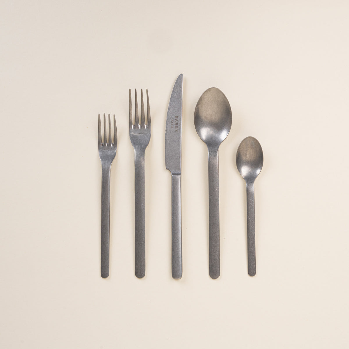 Set of steel matte cutlery including forks, knife, and spoons on a beige background