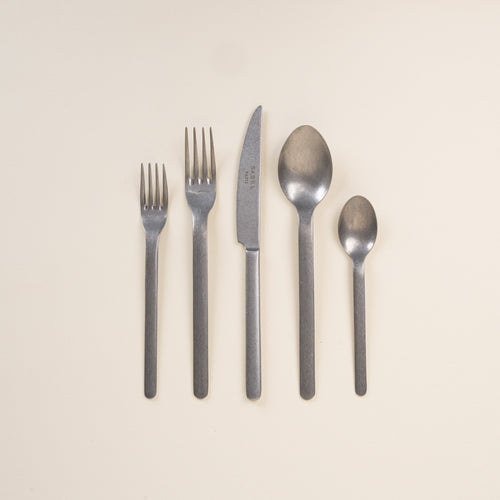 Set of steel matte cutlery including forks, knife, and spoons on a beige background
