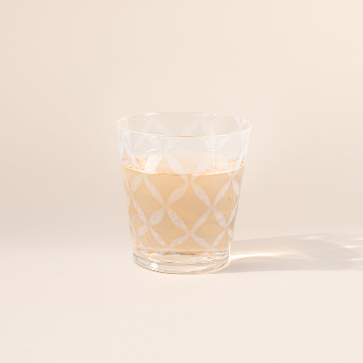 A short clear glass with a delicate grid pattern, half filled with a drink