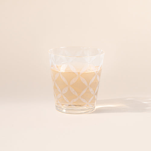 A short clear glass with a delicate grid pattern, half filled with a drink