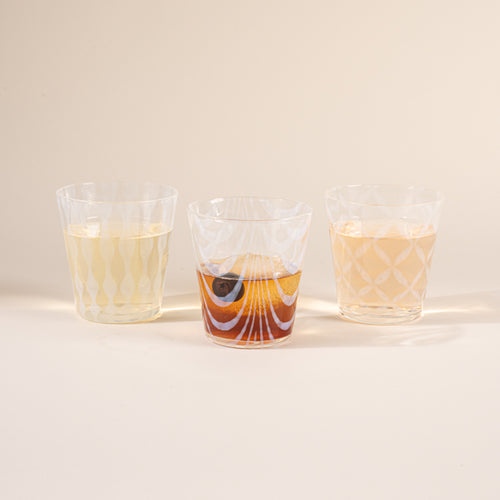 Three glasses half filled with delicate patterns and cascading shadows, filled with drinks