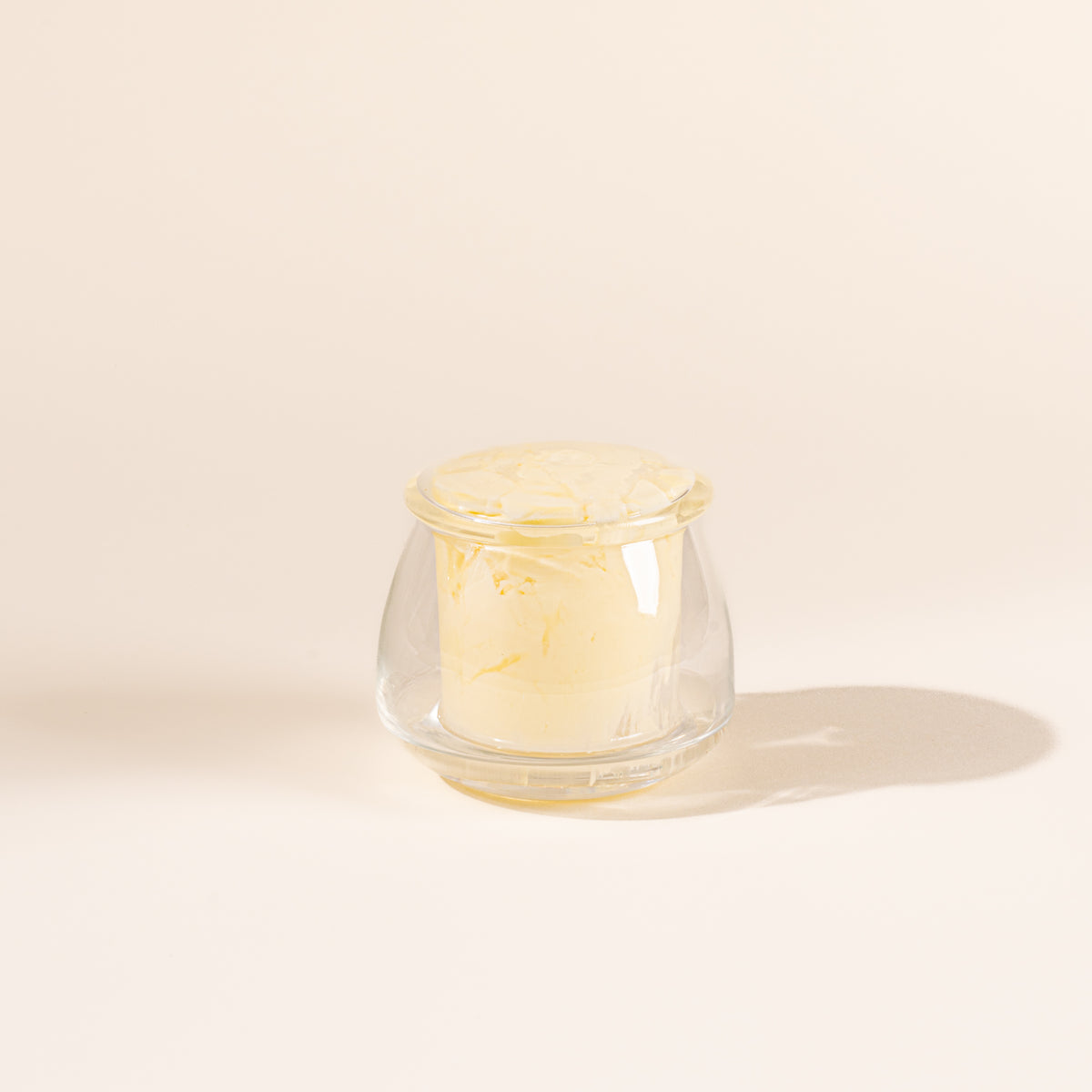 Clear glass butter keeper on white background, filled with butter