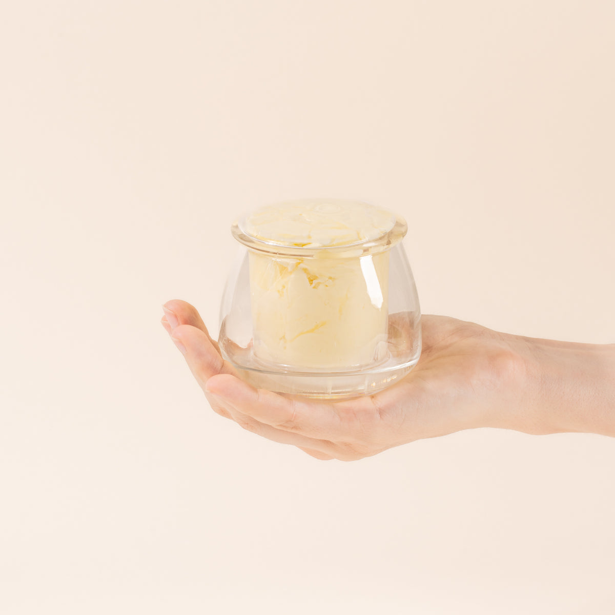 Hand holds a clear glass butter keeper, filled with butter.
