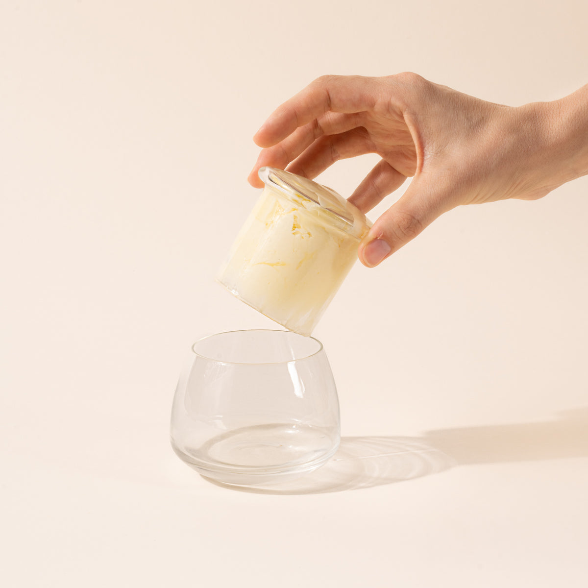 A hand holds the top of the clear butter keeper filled with butter, over the rounded base.
