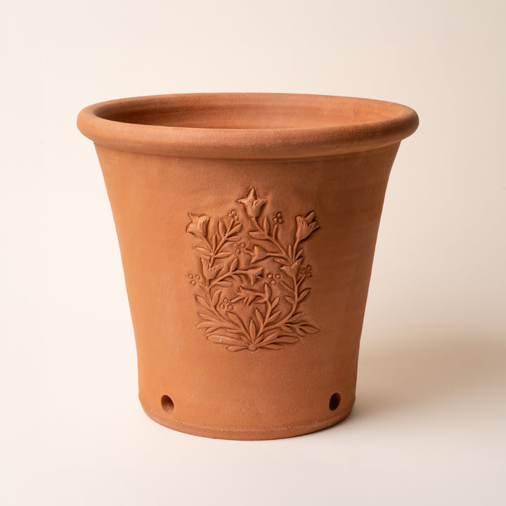 Terracotta flower pot with embossed floral design and drainage holes against a light background.