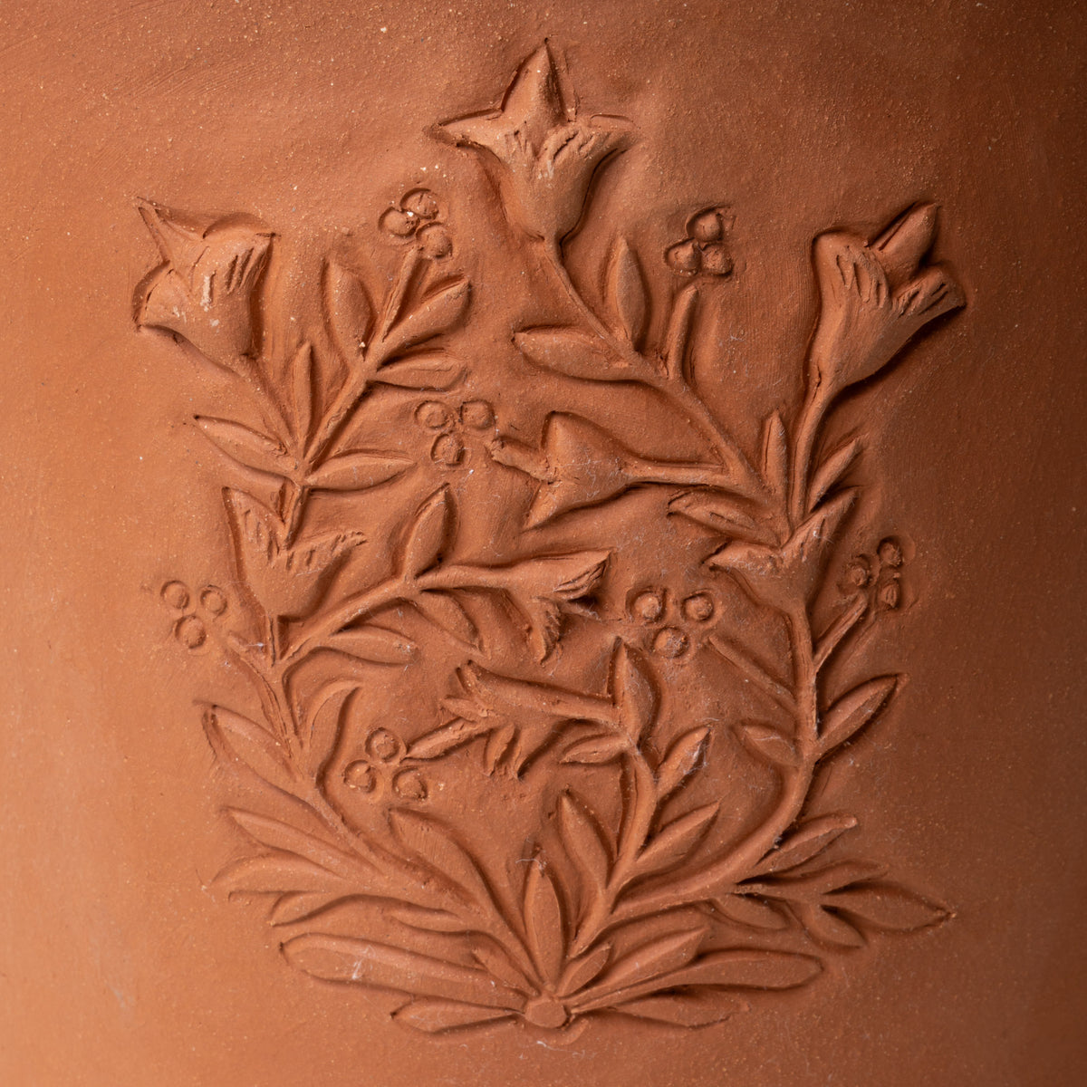 Close up of an embossed floral design on a large terracotta flower pot.