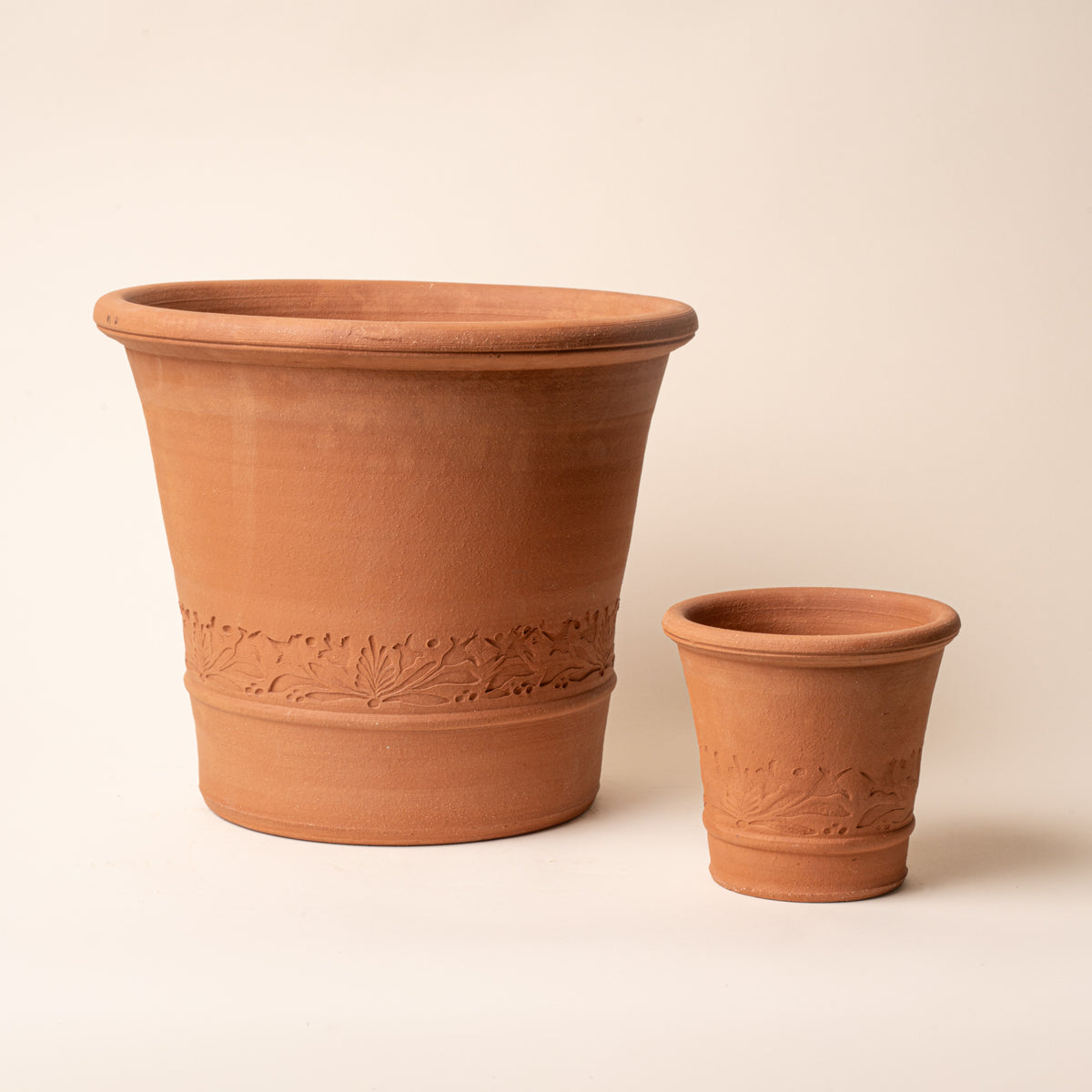 Large and small terracotta planters with embossed botanical detailing displayed against a neutral background.
