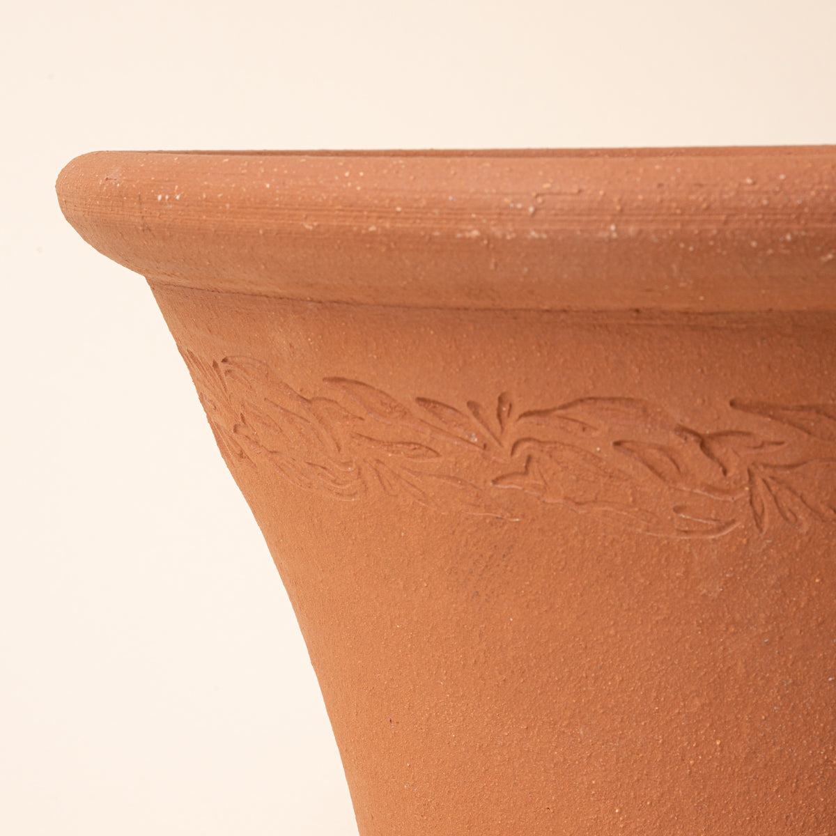 Closeup of a terracotta pot with embossed design on a beige background