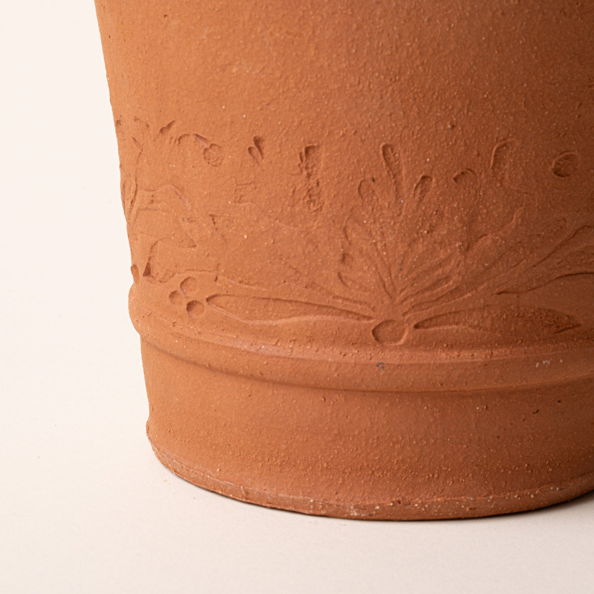 Close-up of a small terracotta pot with floral embossing on a beige background