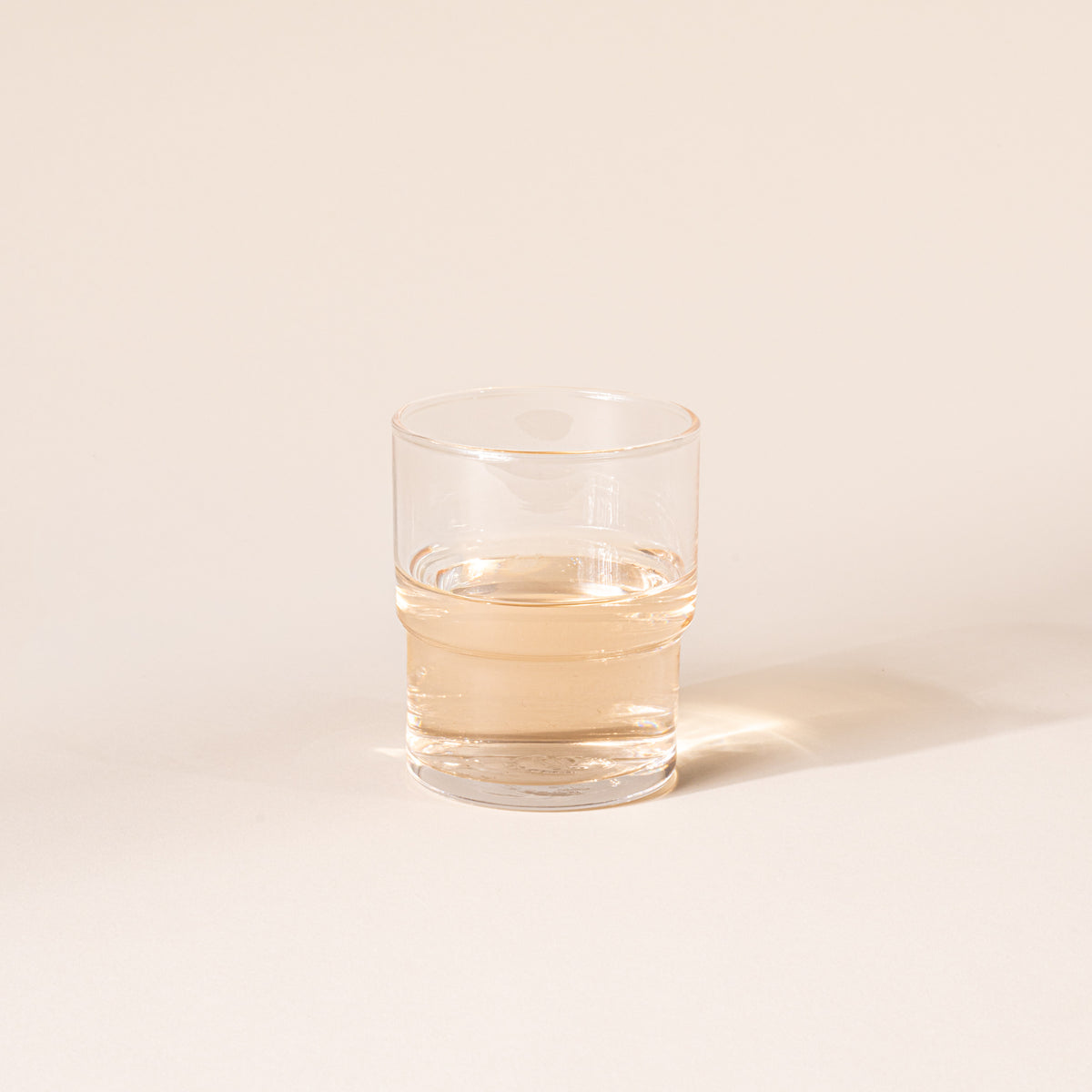 Clear cylindrical glass with a wider top half with a narrower bottom half, filled with a drink.