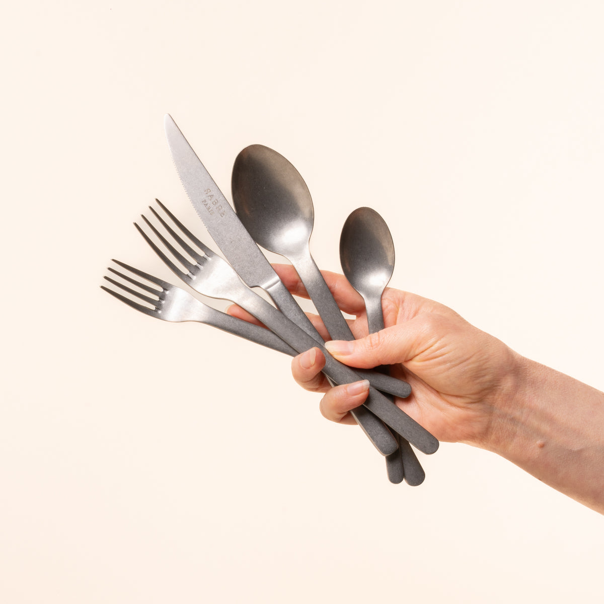 Hand holding a set of silver cutlery against a white background