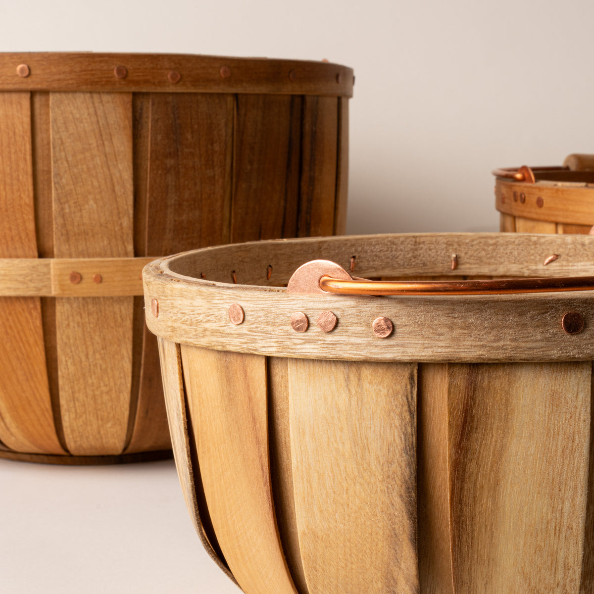 Close-up of wooden bushel baskets with copper rivets and handles, showing varied wood grain and slatted construction.