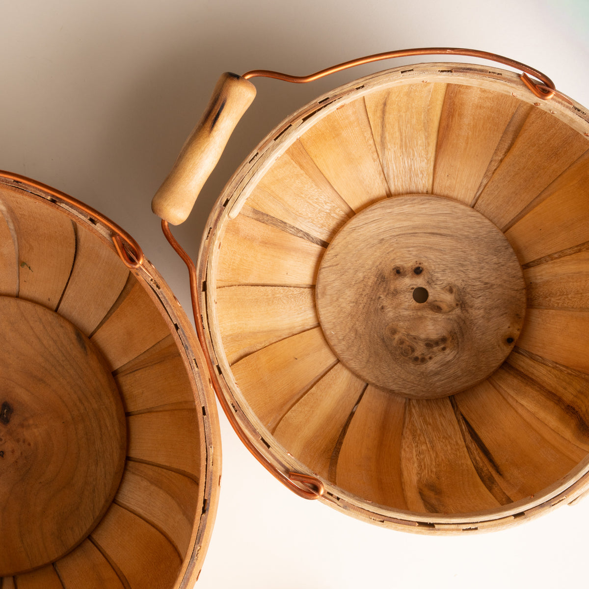 Top-down view of two wooden bushel baskets showing slatted interiors, copper handles, and circular wood bases.