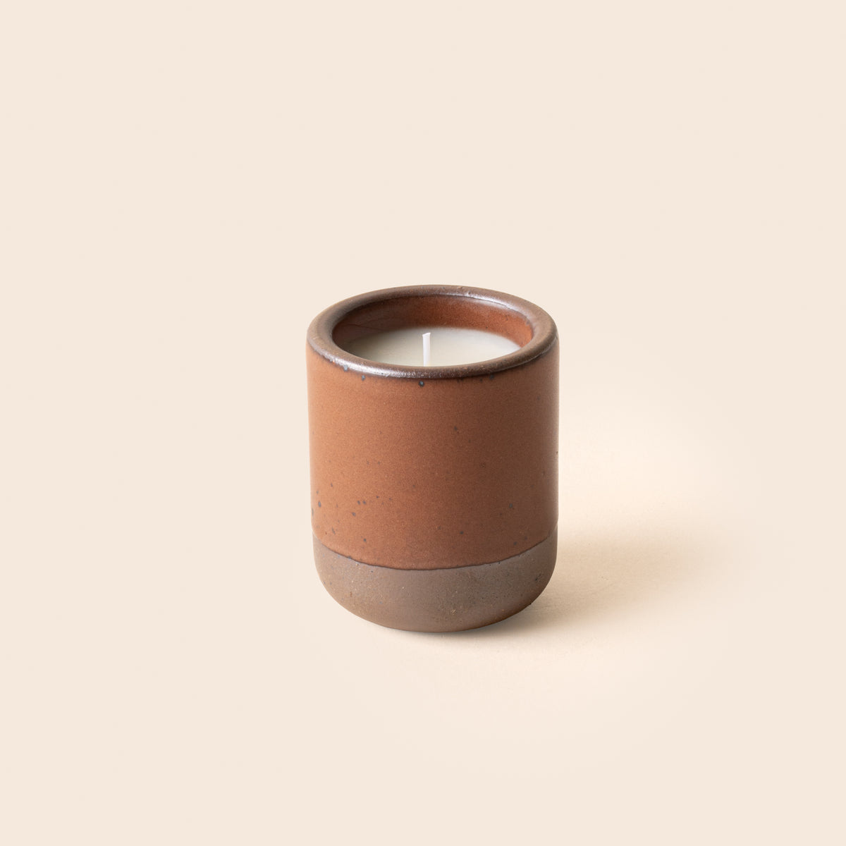 Small ceramic vessel in a cool terracotta color with candle inside.