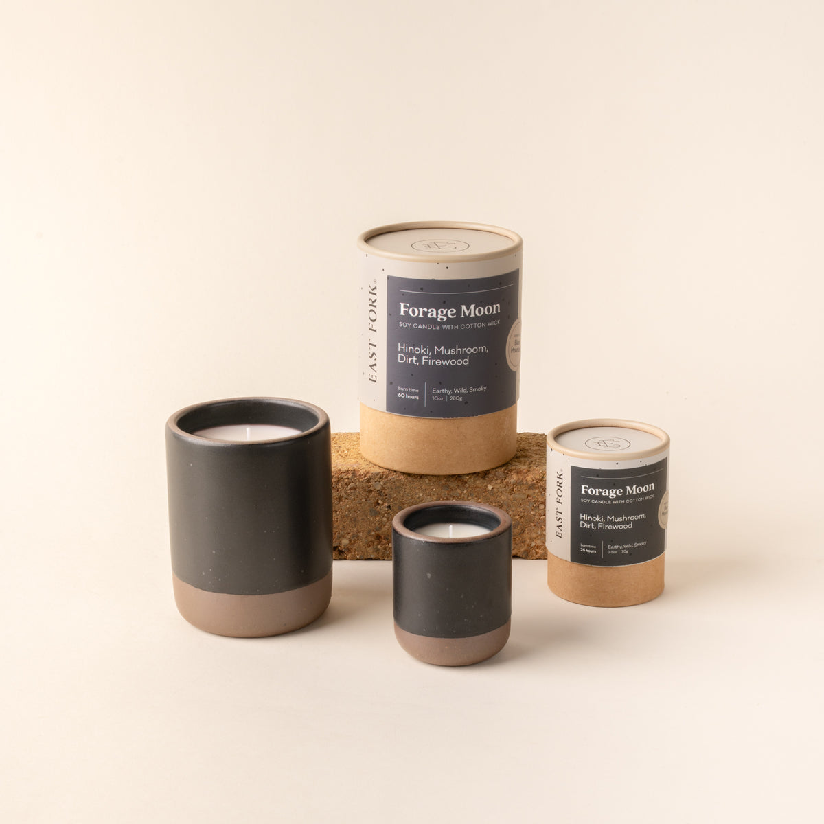 Small and large ceramic vessel in a black color with candles inside, arranged with tube packaging that reads 'Forage Moon'