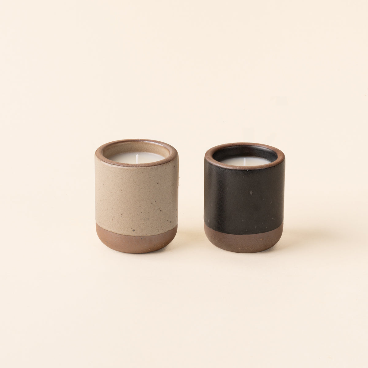 Two small ceramic vessels in warm pale brown and graphite black colors with candles inside each.