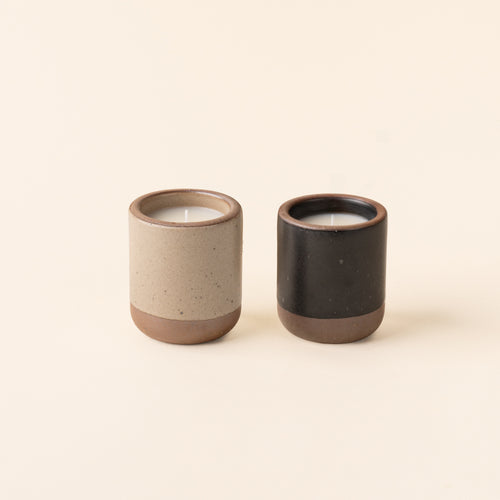 Two small ceramic vessels in warm pale brown and graphite black colors with candles inside each.