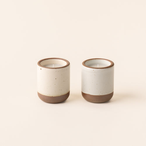 Two small ceramic vessels in cream off-white and cool white colors with candles inside each