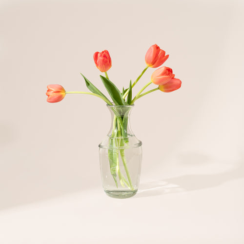 Clear glass bottle vase with a flared neck and decorative ring detail, filled with water and flower stems.
