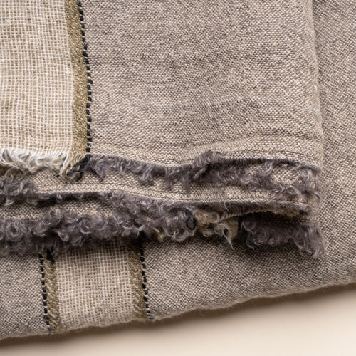 Closeup of a soft gray linen tablecloth with cream and olive woven stripes and fringed edges, neatly folded on a clean neutral background.