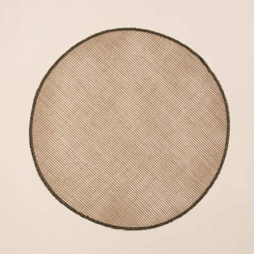 Round woven placemat in a natural color with a sewn olive green rim on a beige background