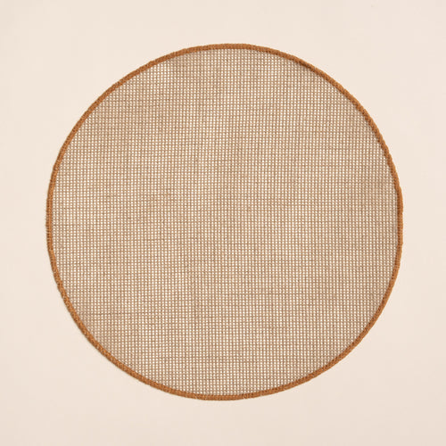 Round woven placemat in a natural color with a sewn rust rim on a beige background