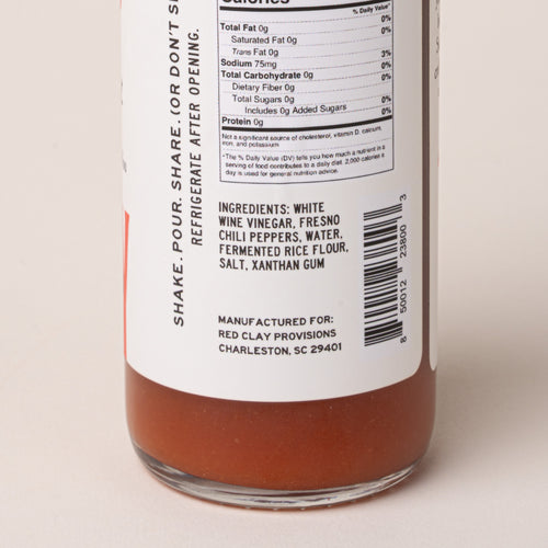 Close-up of the back label of a glass bottle containing an orange-brown liquid, showing nutrition facts, ingredients, and a barcode on a white label.