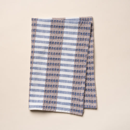 Folded woven kitchen towel with blue and beige striped pattern on a light background.