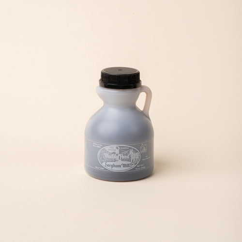 Bottle of Muddy Pond Sorghum Mills pure sorghum syrup with black cap on a plain white background.