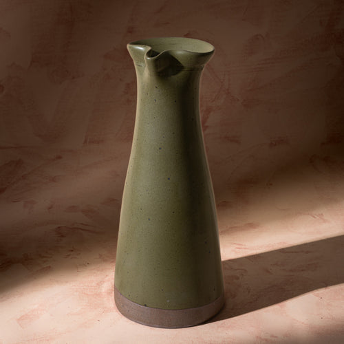 Tall ceramic carafe in an olive green color with iron speckles and an unglazed base.