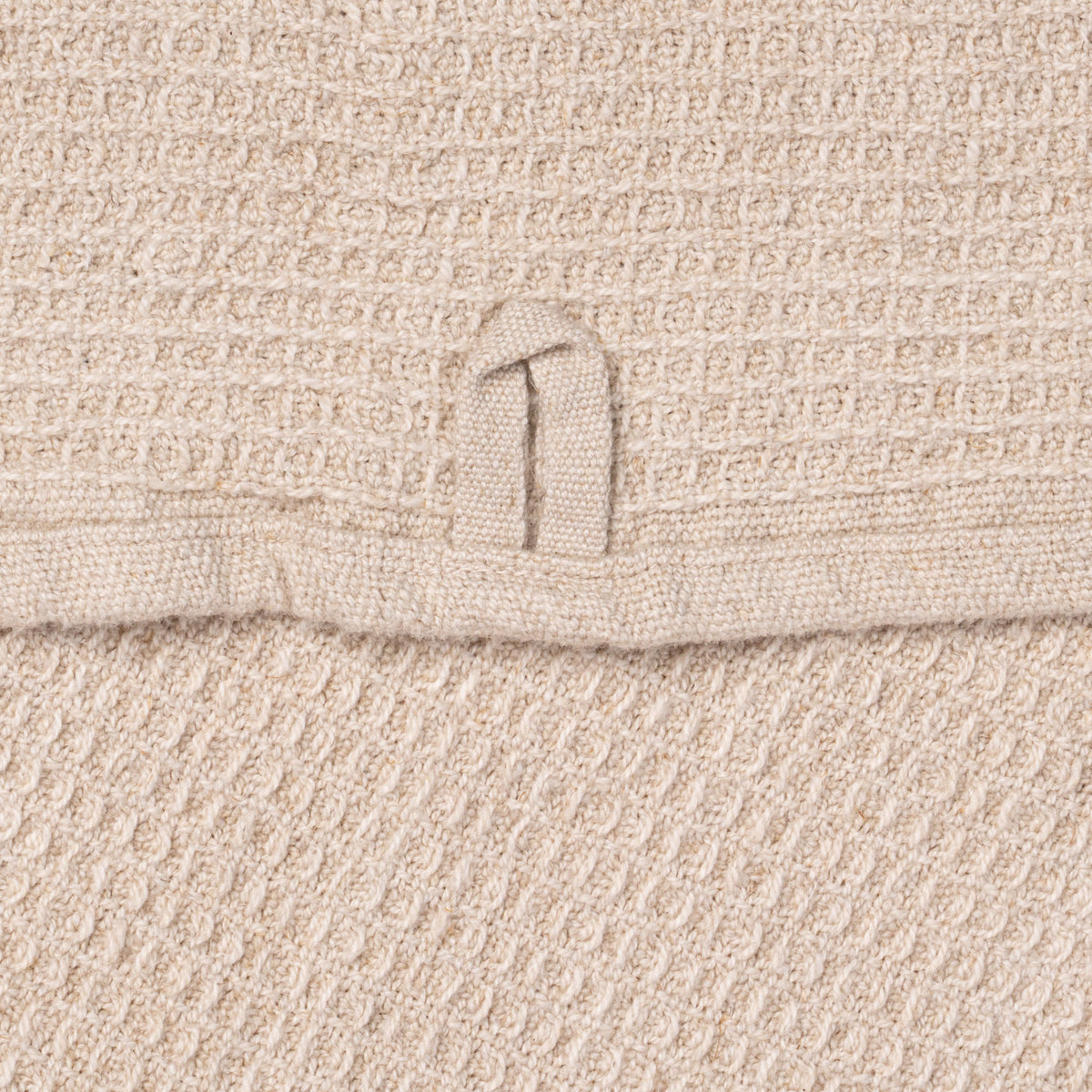 A closeup of a natural waffle weave kitchen towel, with a hanging loop.