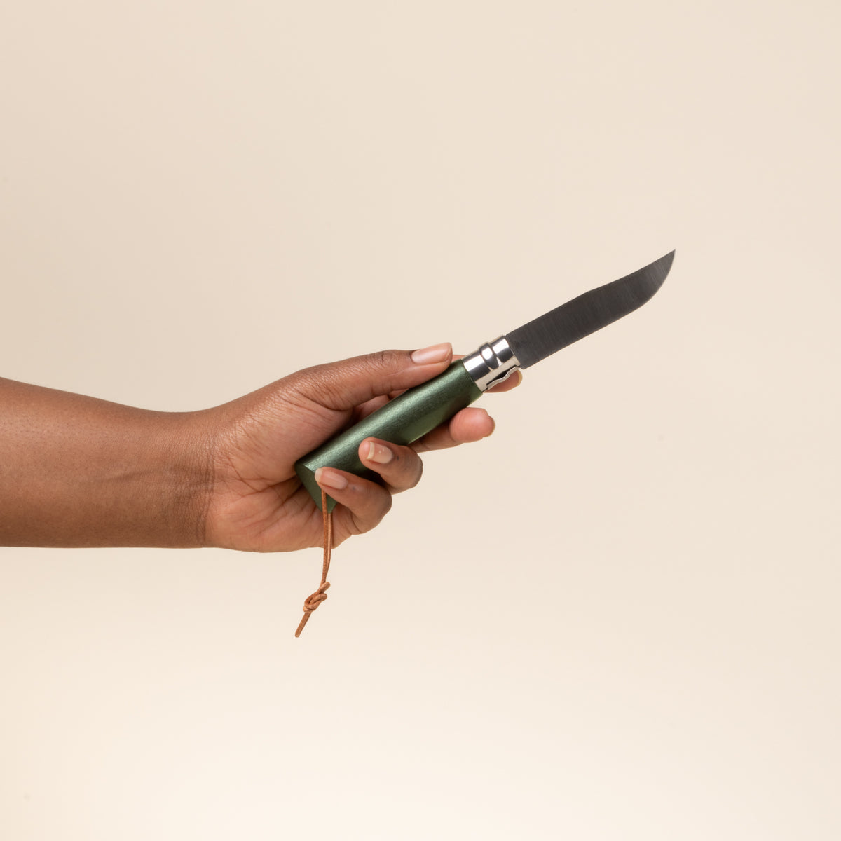 A hand holds a green-handled folding knife with stainless steel blade and leather lanyard.