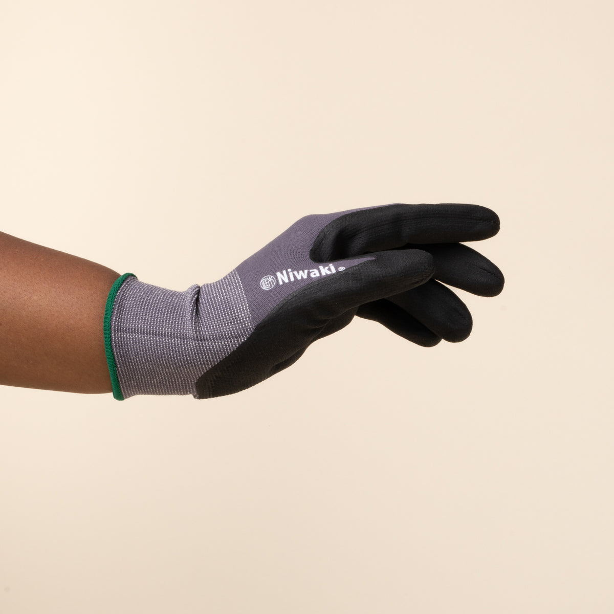 A hand wears a gray and black gardening glove with green trim.